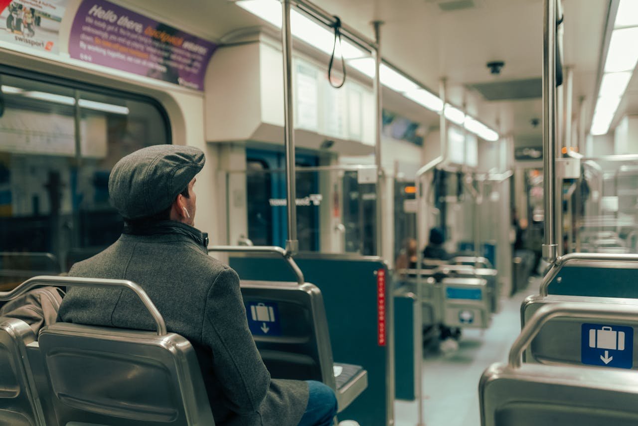 A man in a cap and coat sits inside a modern subway train car.